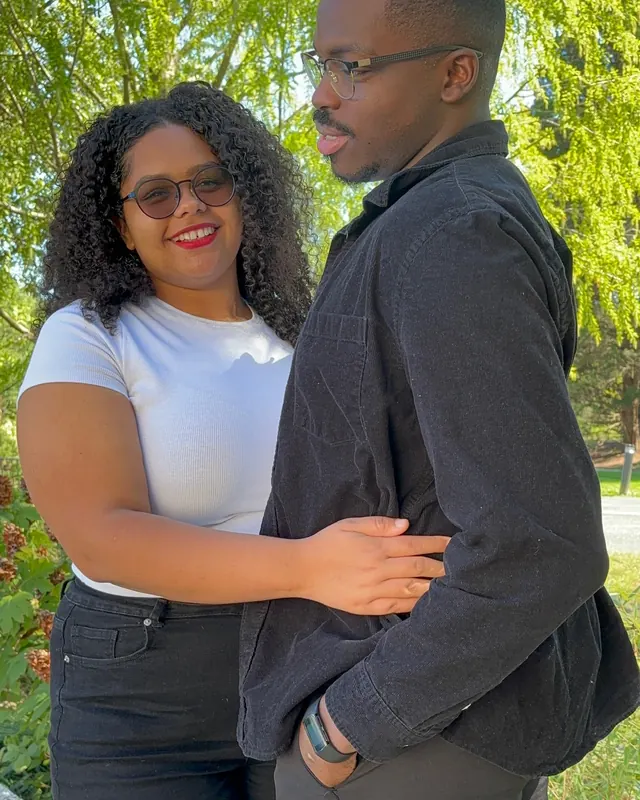 Nicole, smiling, holds Timothy’s arm in a sunlit garden.